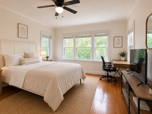 A bedroom with a bed, a desk, a chair, a television, and a ceiling fan.