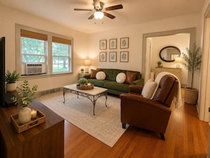 A living room with a green sofa, a brown armchair, a coffee table, and a ceiling fan.