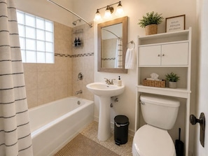 A bathroom with a bathtub, sink, mirror, toilet, and shelves with toiletries.