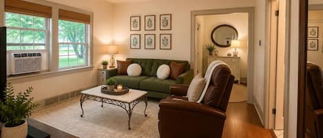 A living room with a green sofa, a brown armchair, a coffee table, and a ceiling fan.