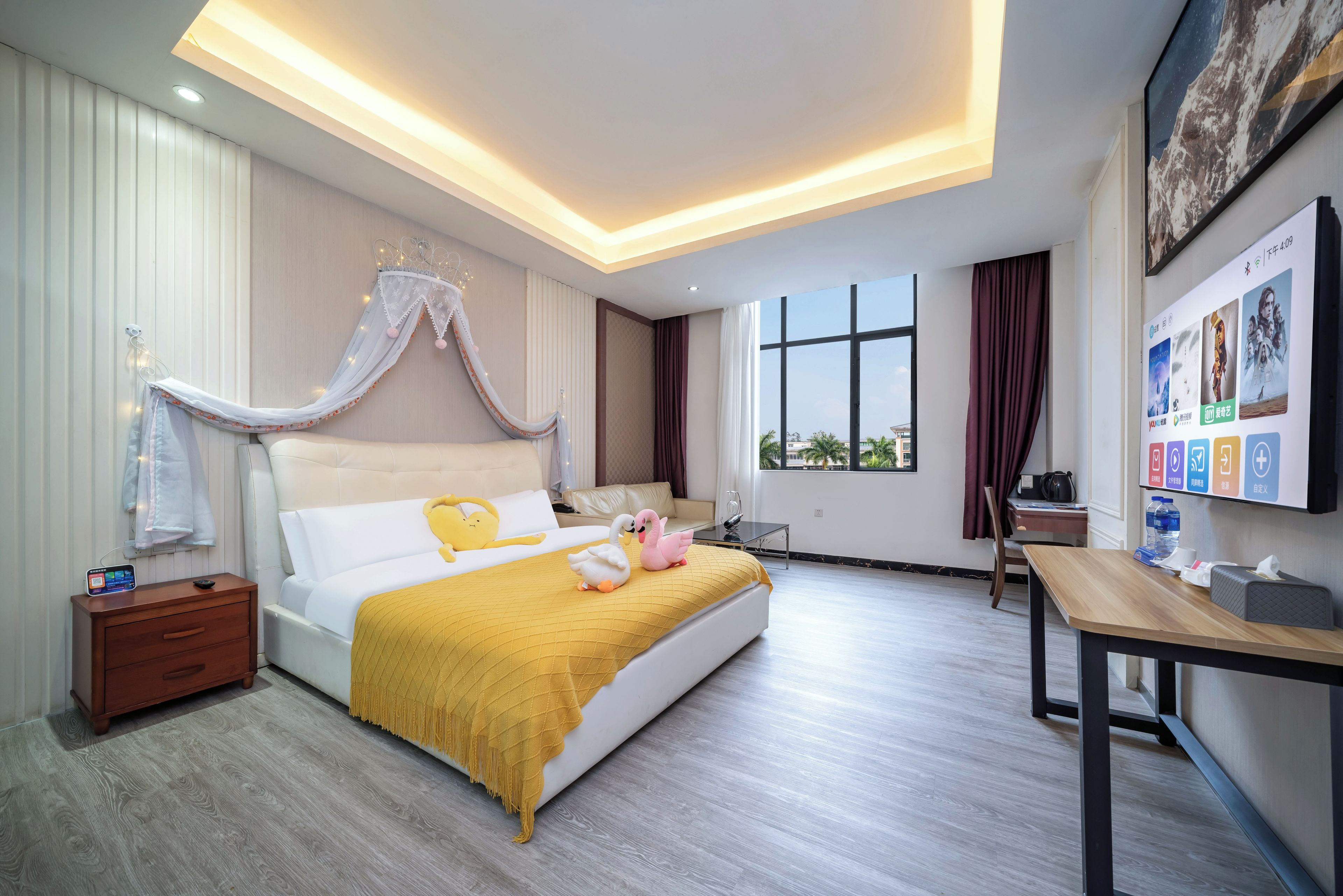 Habitación de hotel con cama, escritorio, silla, mesita de noche y televisor montado en la pared.