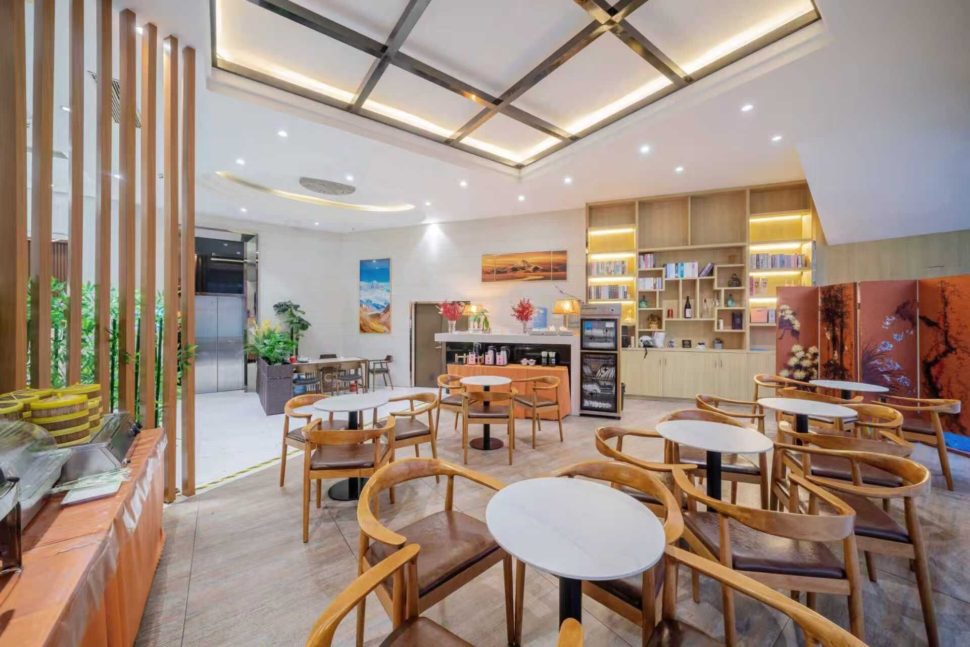 Una cafetería moderna con muebles de madera, un área de estar central y una estantería con libros y objetos decorativos.