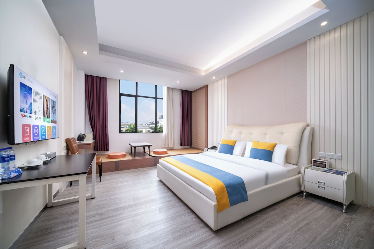 Ein modernes Hotelzimmer mit einem großen Bett, einem Schreibtisch, einem Stuhl, einem kleinen Tisch und einem an der Wand befestigten Fernseher.