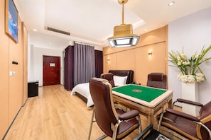 Habitación de hotel con mesa de billar, sillones de cuero, cama con cabecera blanca y un ventanal con cortinas.