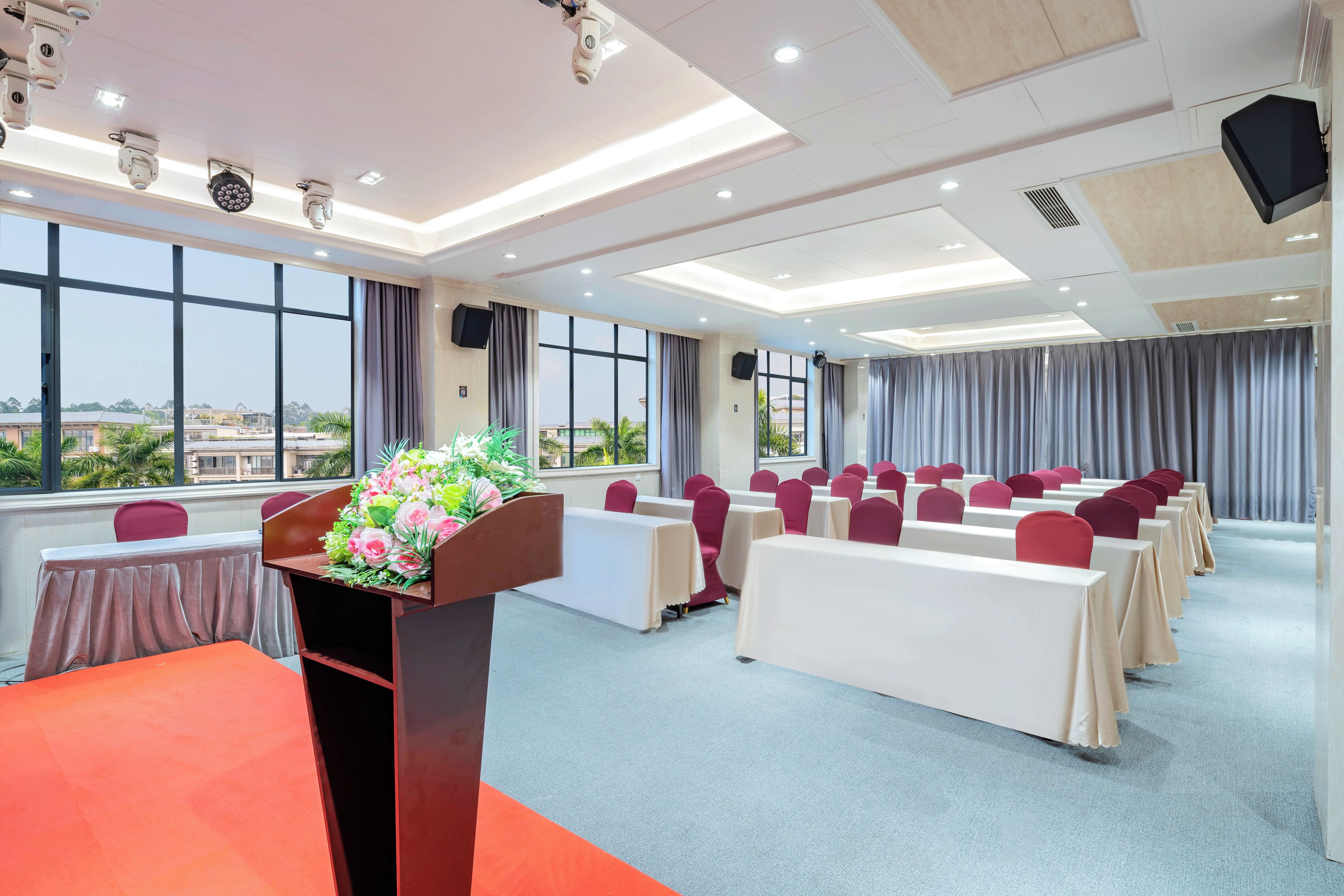 Un salón de conferencias con un atril, mesas, sillas y ventanas amplias.