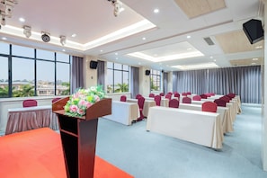 Un salón de conferencias con un atril, mesas, sillas y ventanas amplias.