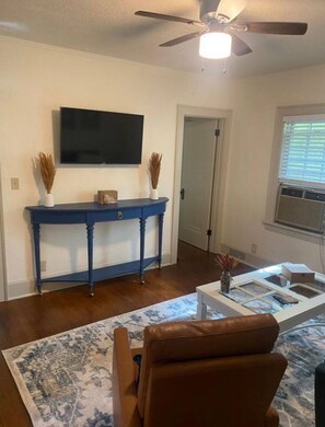 A living room with a television mounted on the wall, a blue console table, a brown leather chair, and a patterned rug.