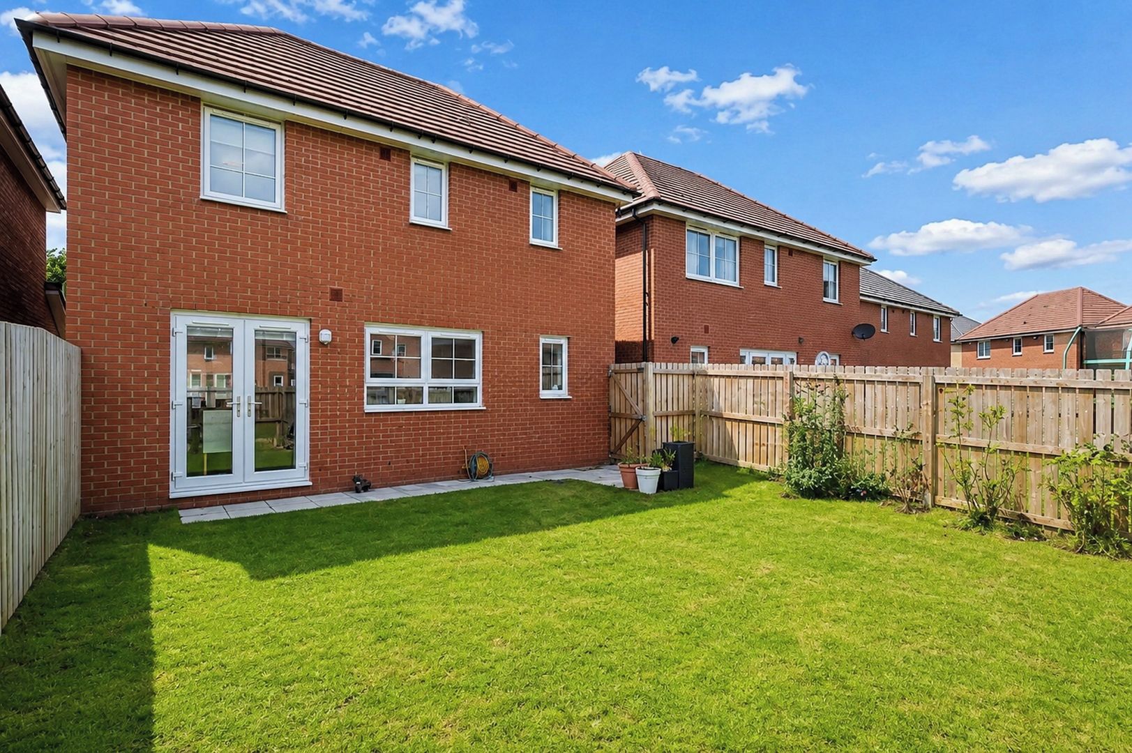 A two-story brick house with a fenced backyard, a sliding glass door, and a well-maintained lawn.