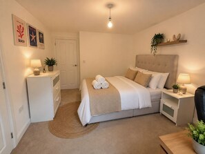 Une chambre bien rangée, avec un lit, des tables de chevet, un petit bureau et une porte.