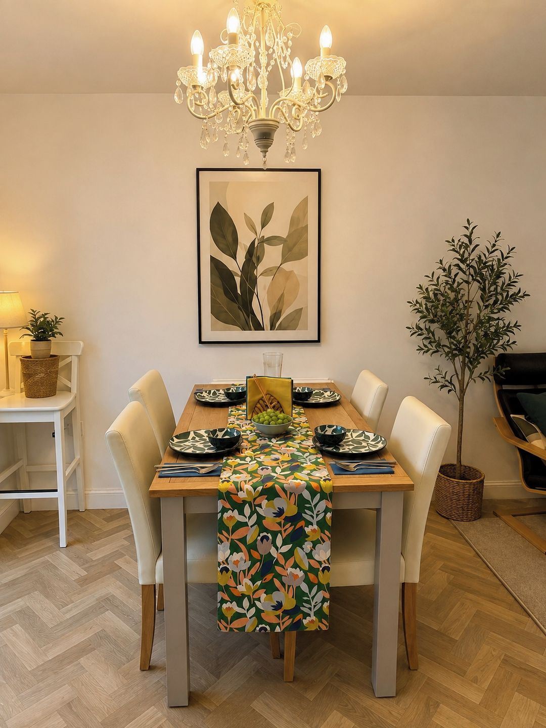 A dining area with a chandelier, a framed plant, and a table set with plates and a bowl.