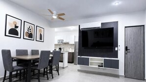 Ein modernes Wohnzimmer mit Essbereich, einem Wand-Fernseher und einem Deckenventilator.