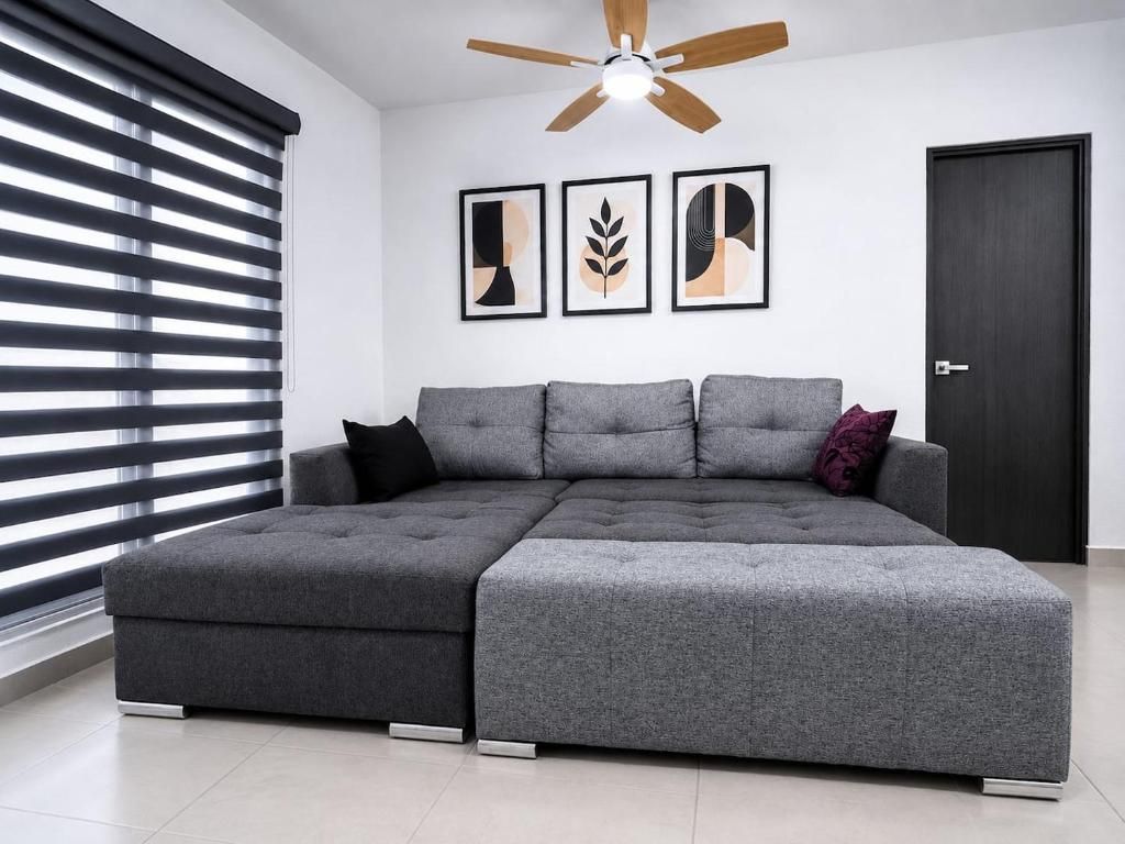 A modern living room with a sectional sofa, a ceiling fan, and abstract wall art.