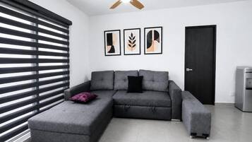 A modern living room with a sectional sofa, a ceiling fan, and a door.