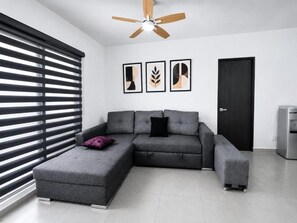 A modern living room with a sectional sofa, a ceiling fan, and a door.