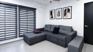 Ein modernes Wohnzimmer mit einem grauen Ecksofa, einem kleinen Hocker und einem Deckenventilator.