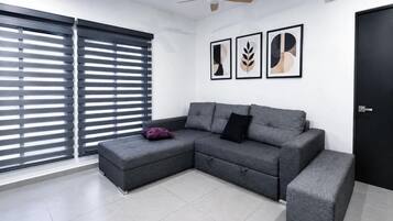 A modern living room with a grey sectional sofa, a small ottoman, and a ceiling fan.
