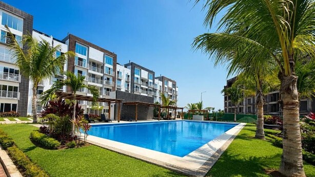 Ein Swimmingpool, umgeben von gepflegtem Rasen und Palmen, mit modernen Gebäuden im Hintergrund.