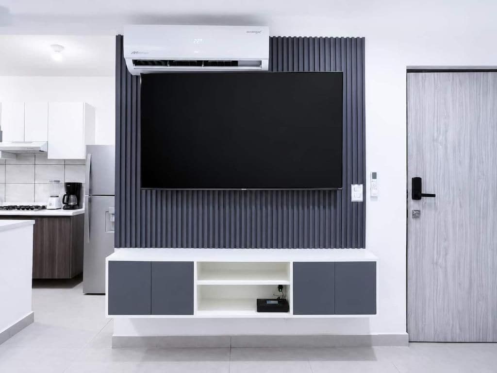 Una cocina moderna con televisor integrado, armarios grises y una puerta de madera.