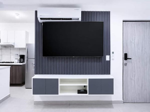 A modern kitchen with a built-in TV, grey cabinetry, and a wooden door.