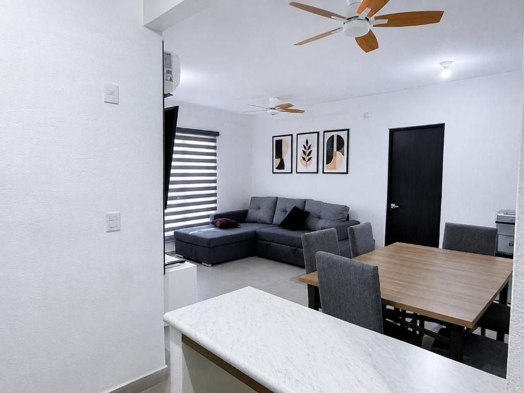 Una sala moderna con un sofá seccional, una mesa de comedor con sillas, ventiladores de techo y obras de arte colgadas en la pared.