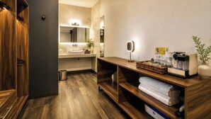 Ein modernes Badezimmer mit einem Holzkosmetikschrank, einem Waschbecken, einem Spiegel und einer Kaffeemaschine.