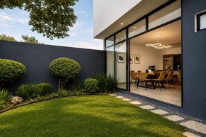 A modern house with a well-maintained lawn, a dining area with chairs, and a kitchen visible through glass doors. - Mura Signature Grand Residence (San Miguel de Allende)