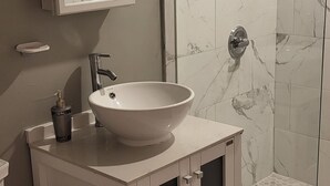 Ein Badezimmer mit einem weißen Waschbecken, einer Toilette, einer Duschkabine aus Glas und einem Spiegel über dem Waschbecken.