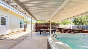 A covered outdoor patio with a hot tub, a table with chairs, and a wooden fence. - Theater, Spa, Gym, & Vinyls: 2 Homes, 1 Epic Stay! (Austin)