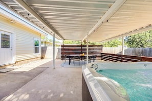 A covered outdoor patio with a hot tub, a table with chairs, and a wooden fence. - Theater, Spa, Gym, & Vinyls: 2 Homes, 1 Epic Stay! (Austin)