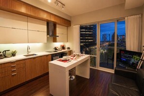 Eine moderne Küche mit einer zentralen Kochinsel, einem Essbereich und einer großen Schiebeglastür, die auf einen Balkon mit Stadtblick führt.