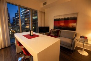 Ein modernes Hotelzimmer mit Essbereich, einer Couch, einem Fernseher und Blick auf die Stadt.