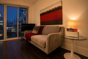 Ein Wohnzimmer mit einer Couch, einem Glastisch, einer Lampe, einem Gemälde und einem Fernseher.
