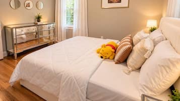 A bedroom with a large bed, a dresser, a window with curtains, and a framed picture on the wall.