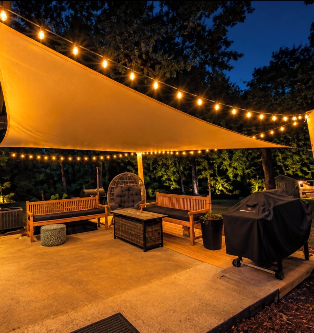 Un área de patio al aire libre con luces colgantes, una zona de estar techada y una parrilla.
