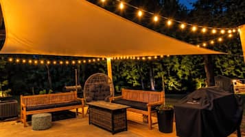 Un área de patio al aire libre con luces colgantes, una zona de estar techada y una parrilla.