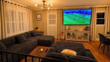 A living room with a large flat-screen TV, dark sofas, a coffee table, and a cabinet with decorative items.