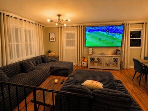 A living room with a large flat-screen TV, dark sofas, a coffee table, and a cabinet with decorative items.
