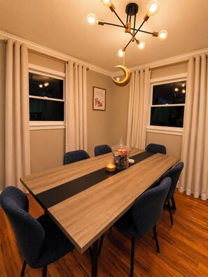 Un comedor con una mesa de madera grande, seis sillas, una lámpara de araña y una lámpara con forma de luna creciente.