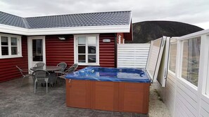 A wooden cabin with a hot tub, a dining area with chairs, and a garage door.