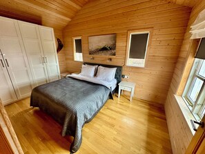 A wooden-paneled bedroom with a bed, a nightstand, a wardrobe, and a window.