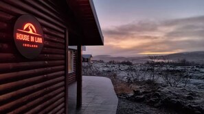 A wooden building with a sign reading 'HOUSE IN LAVA ICELAND' and a view of a snowy landscape.