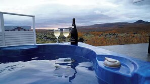 A hot tub with two glasses of white wine and a bottle, set against a scenic view of autumn foliage and mountains.