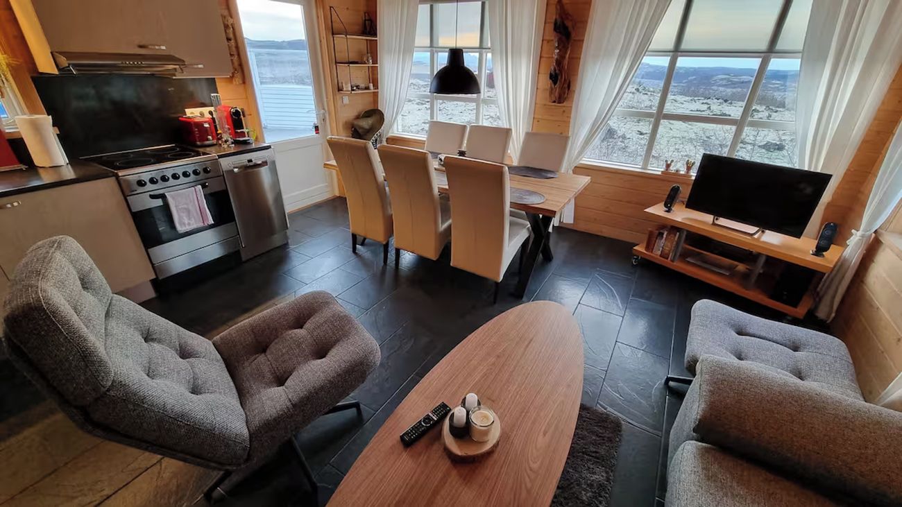 Ett modernt vardagsrum med ett stort fönster, en matplats och ett kök med spis och ugn.