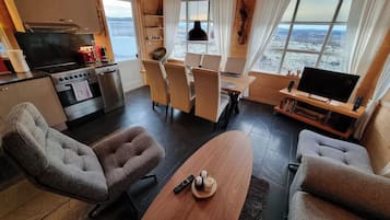 A modern living room with a large window, a dining area, and a kitchen with a stove and oven.