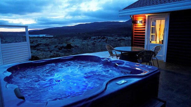 Un jacuzzi con vistas a un paisaje montañoso, una mesa con sillas y una puerta con luz encendida.