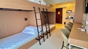 Une petite chambre avec des lits superposés, un bureau et un coin cuisine.