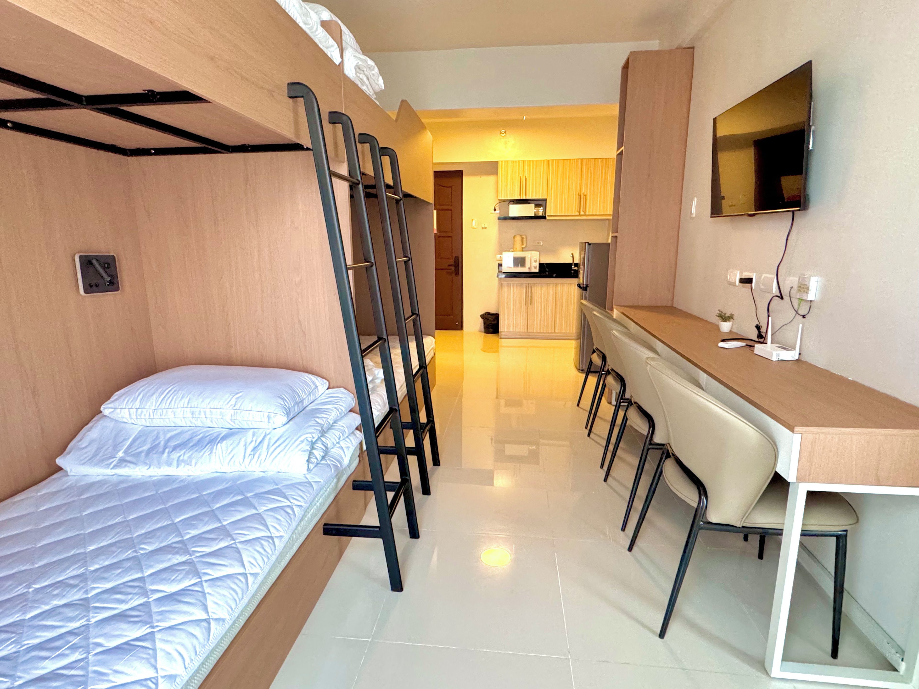 Habitación pequeña con literas, kitchenette y escritorio con sillas.