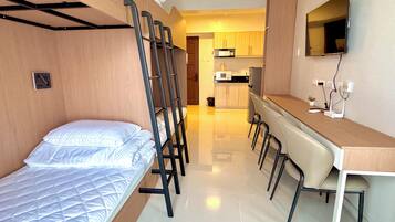 Habitación pequeña con literas, kitchenette y escritorio con sillas.