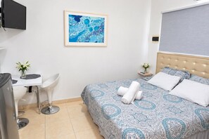 Une chambre d’hôtel avec un lit, un bureau, une chaise, une télévision et une œuvre d’art encadrée au mur.