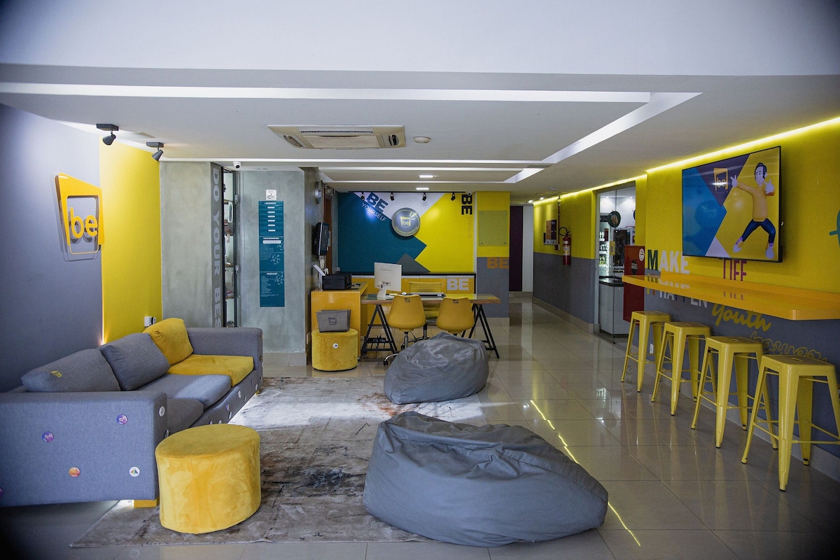 Un interior moderno con un sofá, un reposapiés amarillo y una zona de bar con taburetes.